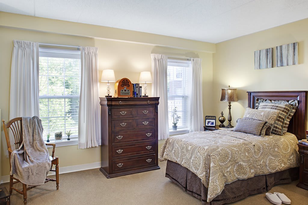 A cozy bedroom with a bed, dresser, and two windows adorned with curtains.