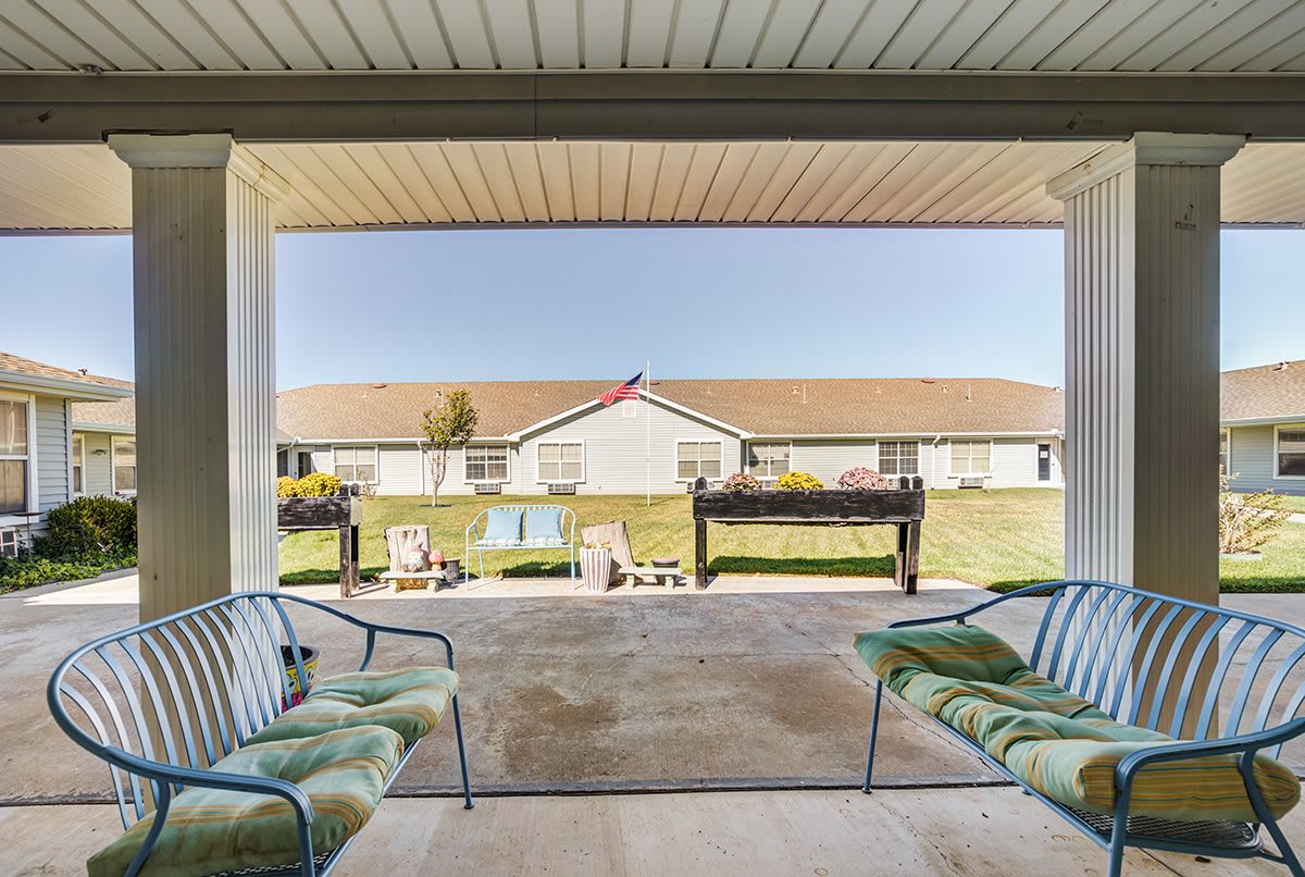 A cozy patio with cushioned chairs overlooks a sunny yard and neighboring building.
