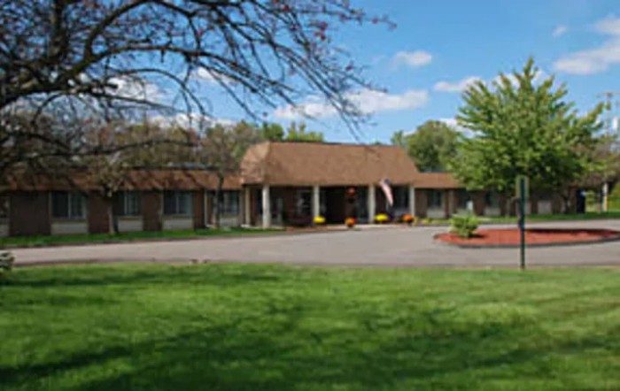 A single-story building surrounded by a lush green lawn and trees under a clear blue sky.