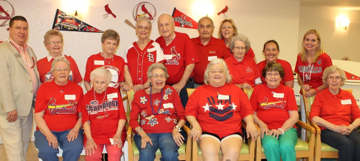A group of elderly people wearing St. Louis Cardinals apparel pose for a photo indoors.