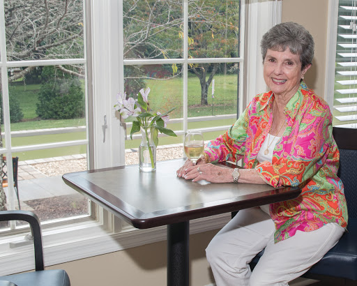 A woman enjoying a drink at a cafe table, surrounded by natural light and flowers.