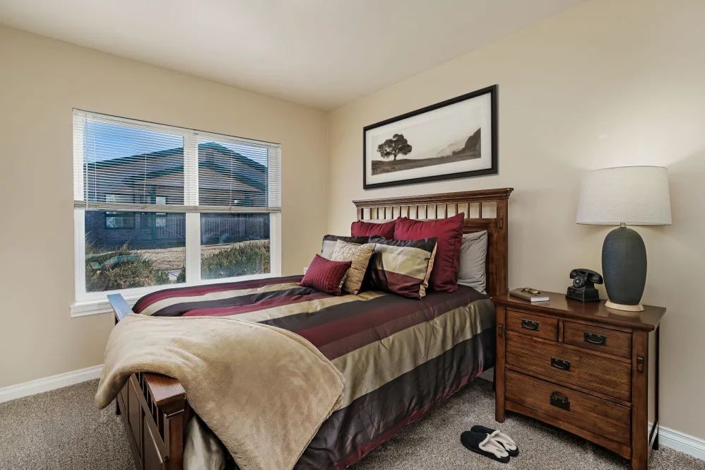 A cozy bedroom with a neatly made bed, bedside table, and large window.