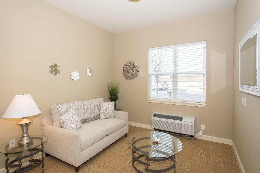 A cozy living room with a beige sofa and glass coffee table, complemented by wall decor and an indoor plant near the window.