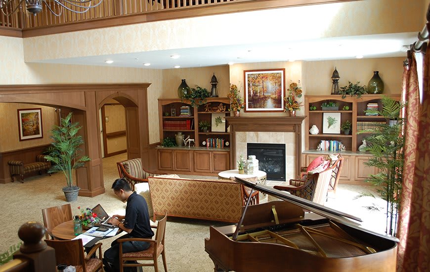 A cozy living room featuring a grand piano, a fireplace, and elegant wooden bookshelves.
