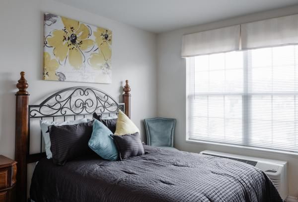 A cozy bedroom featuring a wrought iron bed with decorative pillows, a large window, and floral artwork on the wall.