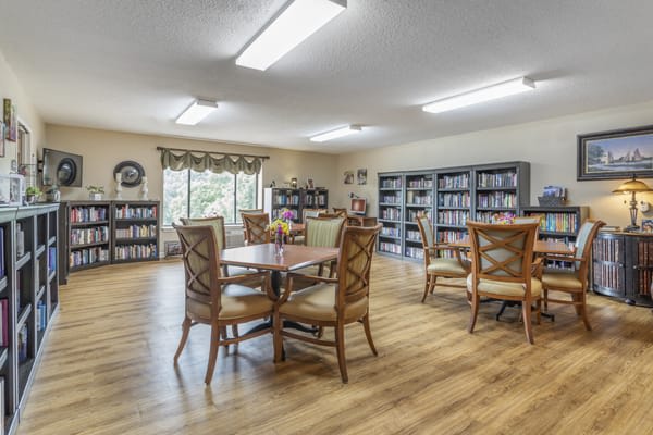 A spacious library room with wooden tables and chairs, lined with bookshelves full of books.