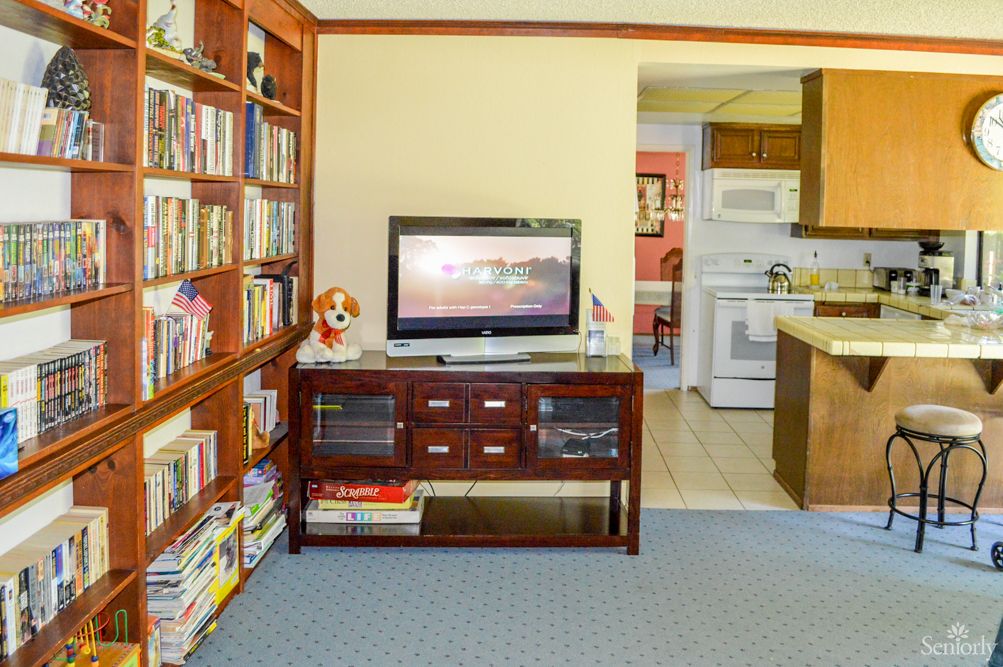 A cozy living room with a bookshelf, television, and a view into the kitchen.
