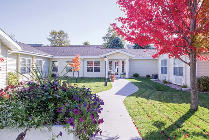 A charming house with a well-maintained garden and a pathway, surrounded by vibrant autumn trees.