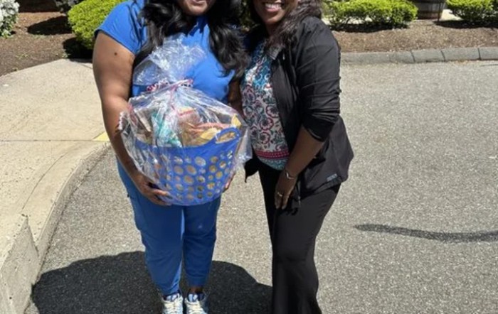 Two people smiling outdoors, holding a gift basket.