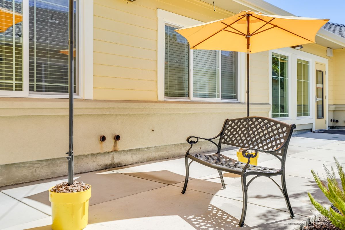 A sunny patio with a metal chair and a yellow umbrella.