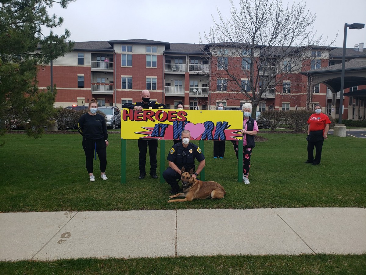 A group of people and a dog posing outdoors with a colorful sign in front of a building.