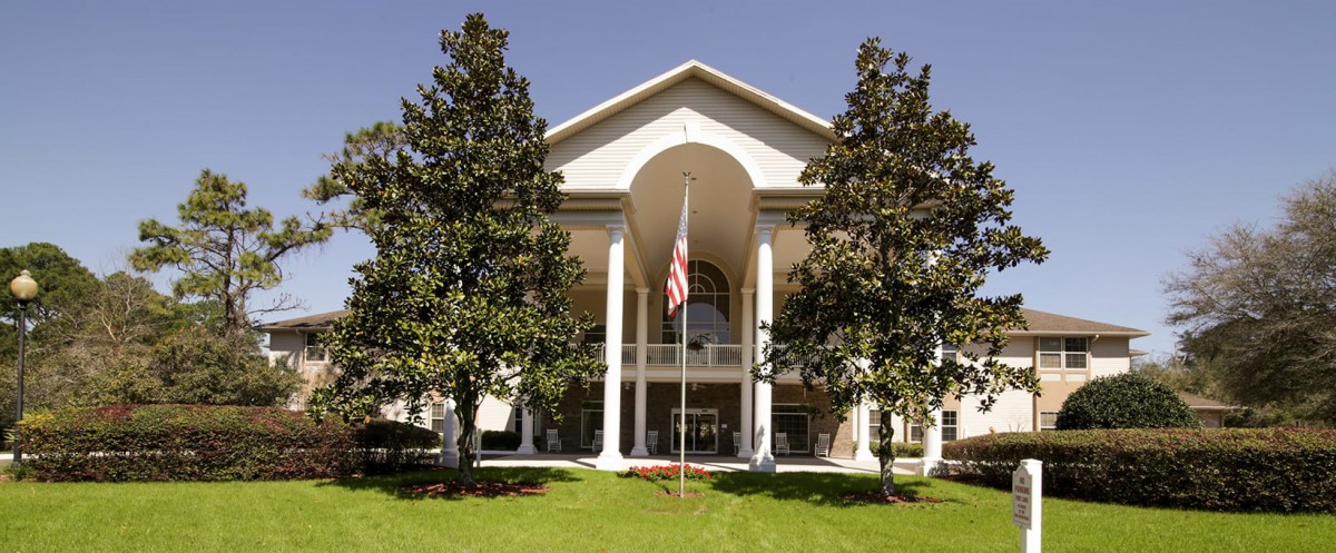 A grand building with large columns and an American flag at the entrance, surrounded by trees.
