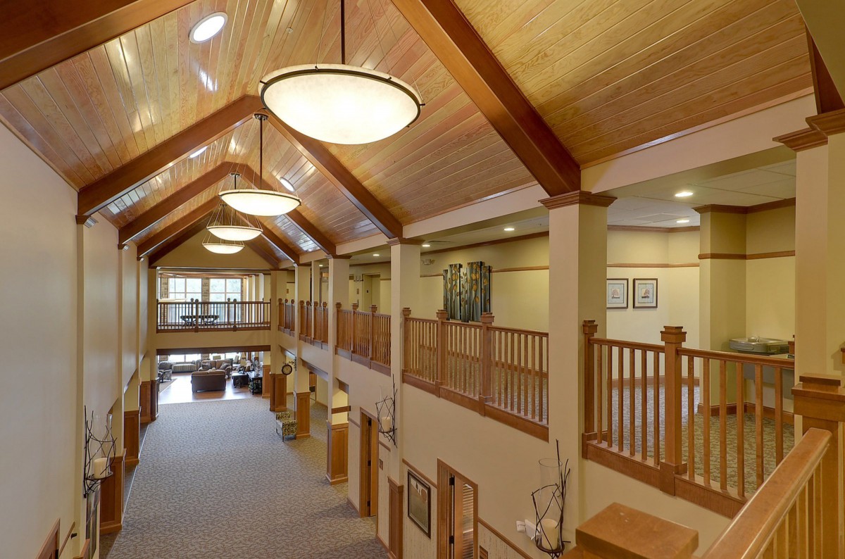 A spacious hallway with wooden ceilings and elegant lighting, featuring a balcony overlooking the area.