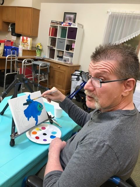 A man engaged in painting on a canvas indoors, with art supplies around him.