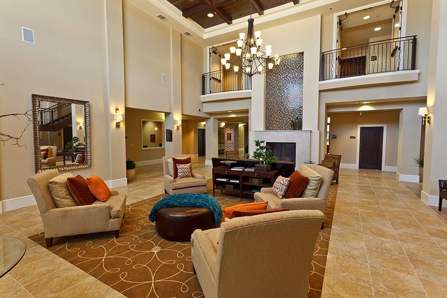 A spacious and elegantly decorated lobby with a central seating area, featuring plush armchairs arranged around a rug beneath a large chandelier.