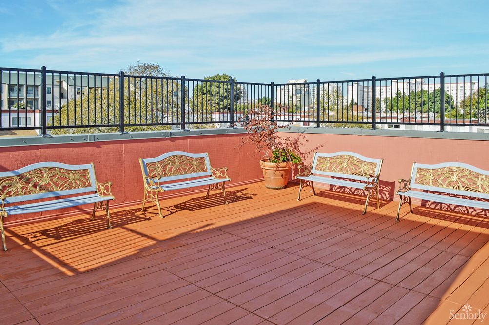 A spacious outdoor patio with wooden benches and potted plants, enclosed by a tall fence.