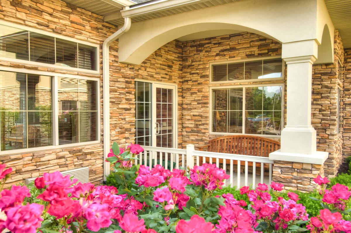 A charming house with a stone exterior and a porch, surrounded by vibrant pink flowers.