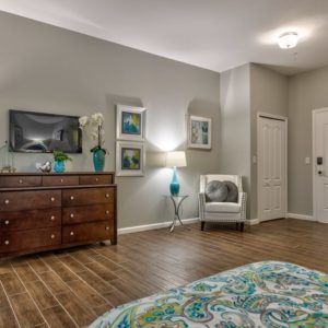 A cozy bedroom featuring a wooden dresser, a mounted TV, a comfortable chair, and elegant decor.