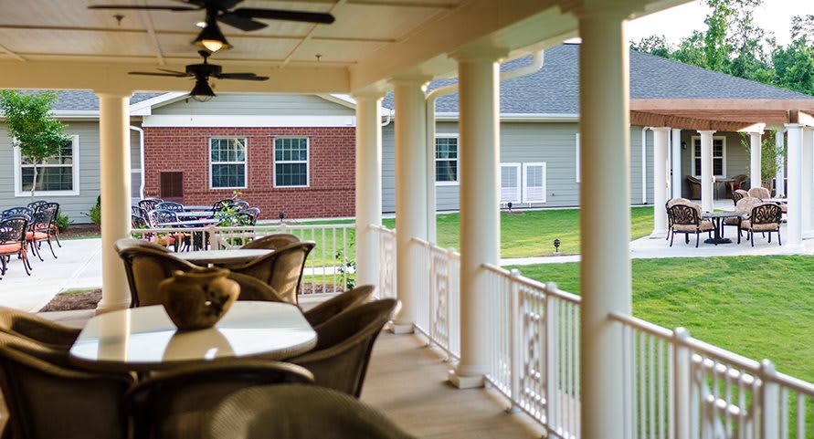 A cozy porch with columns and outdoor seating, overlooking a well-maintained lawn.