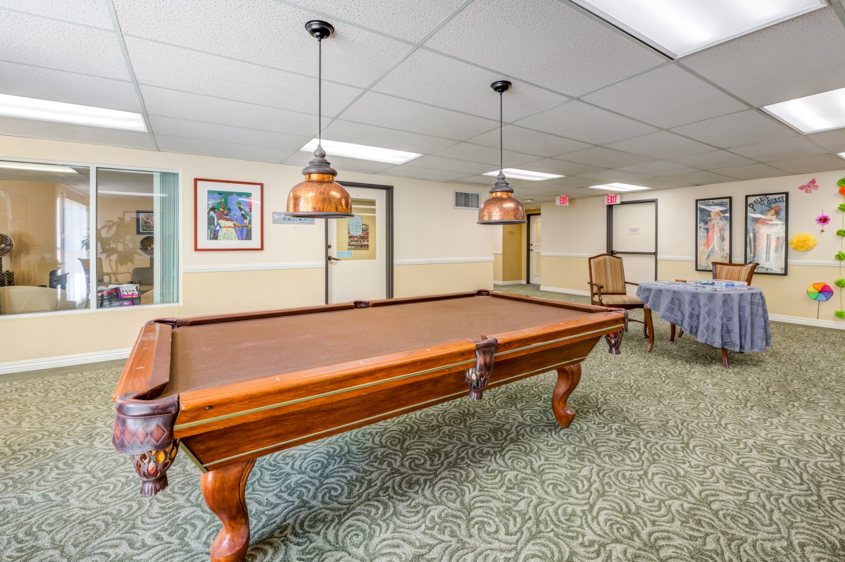 A well-lit game room featuring a classic wooden pool table and overhead pendant lights.