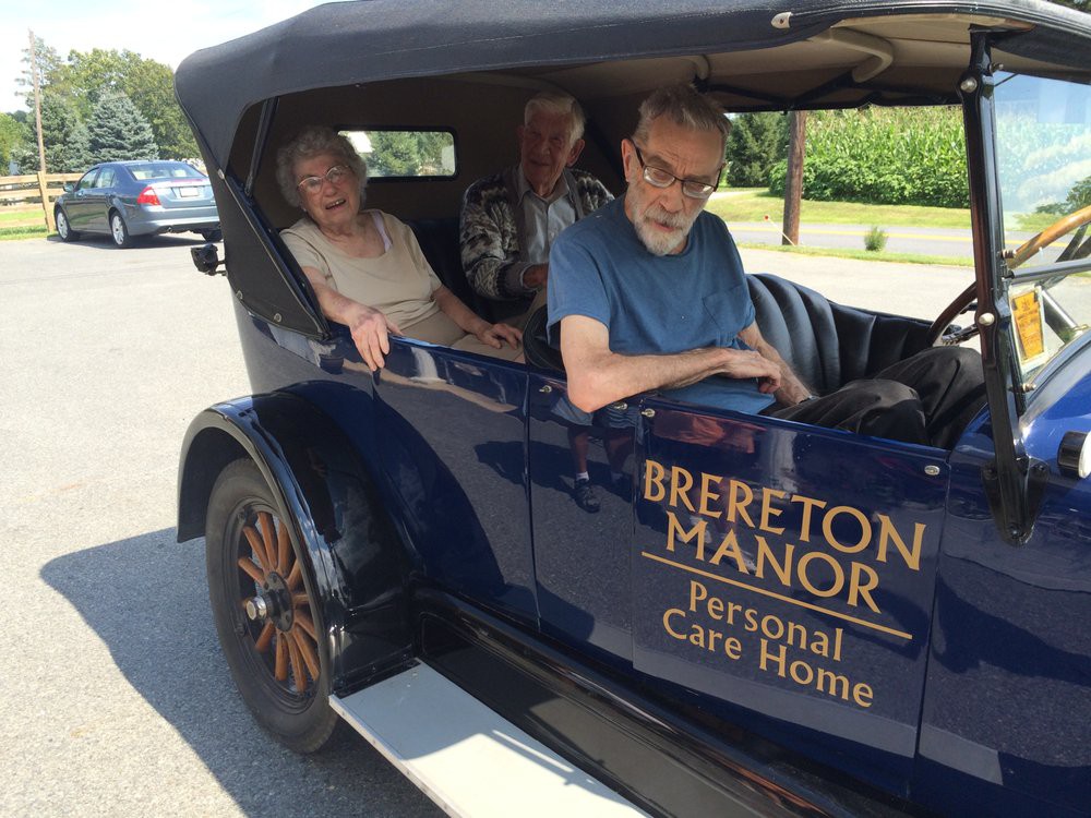 Elderly individuals enjoying a ride in a classic car from Brereton Manor Personal Care Home.