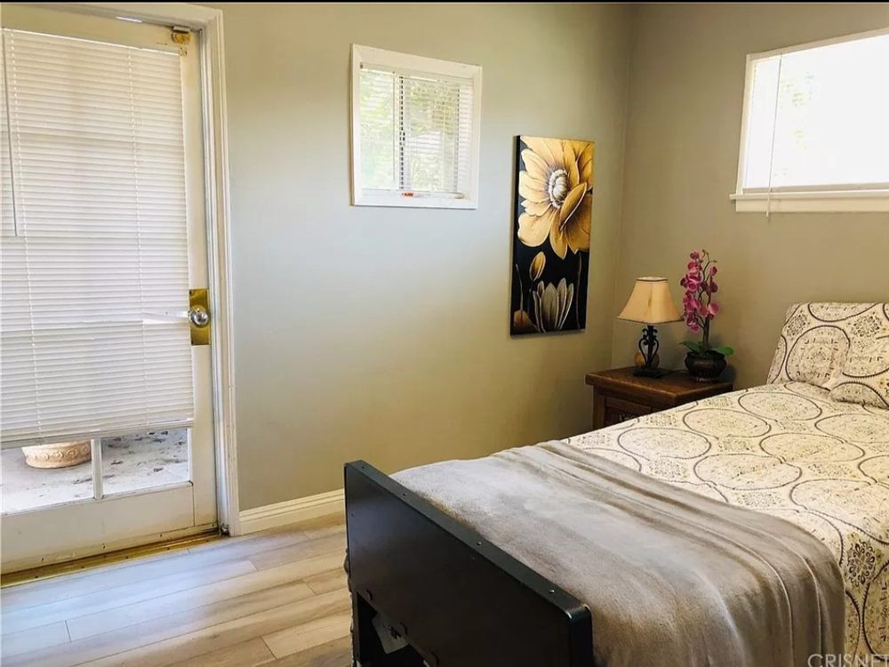 A cozy bedroom with a bed, nightstand, lamp, and wall art near a door and window.