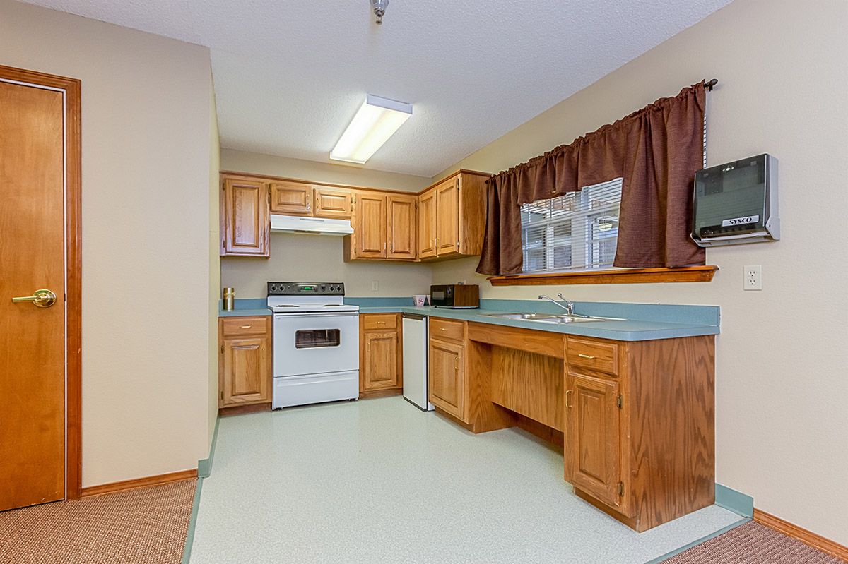 A cozy kitchen featuring wooden cabinets, a stove with an oven, and a window with curtains.
