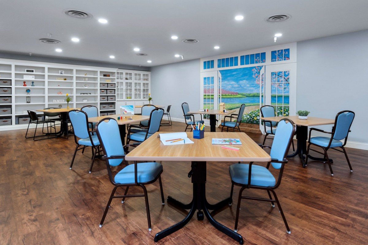 A spacious dining area with multiple tables and chairs, featuring a wall of library shelves and large windows.