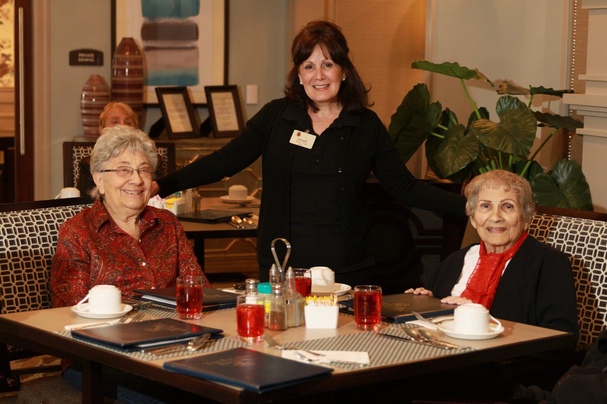 A group of seniors enjoying a meal at a restaurant, accompanied by a staff member.