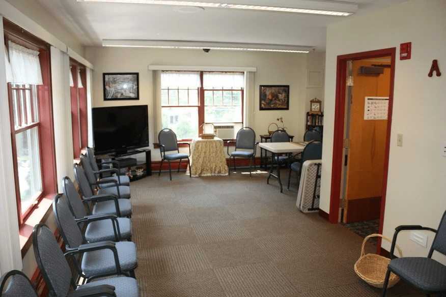 A spacious waiting room with chairs lined up against the walls, a television set, and large windows allowing ample natural light.
