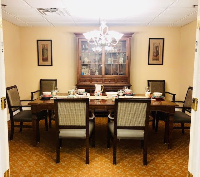 A well-furnished dining room with a chandelier, six chairs around a table, and a cabinet in the background.