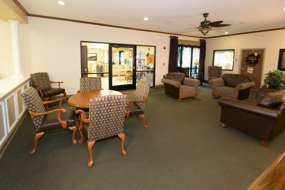 A cozy lounge area with upholstered chairs and a table, featuring a carpeted floor and a ceiling fan.