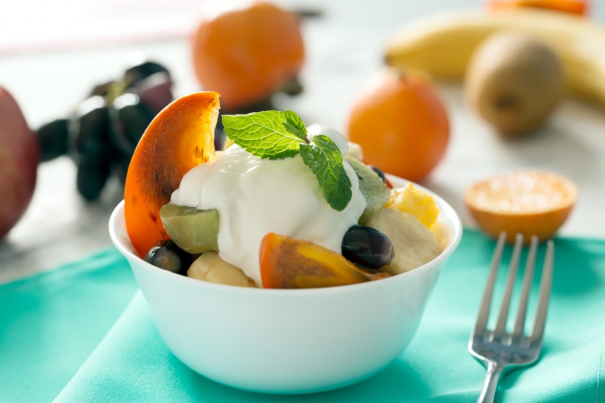 A bowl of fresh fruit salad topped with yogurt and garnished with mint leaves.