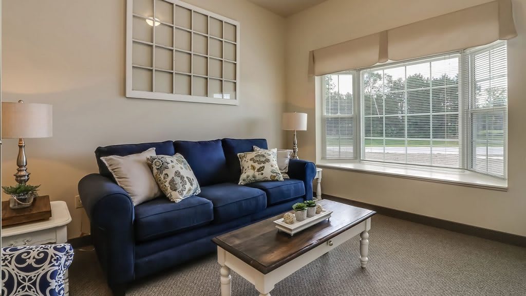 A cozy living room with a blue sofa, decorative pillows, and a modern coffee table beside a large window.