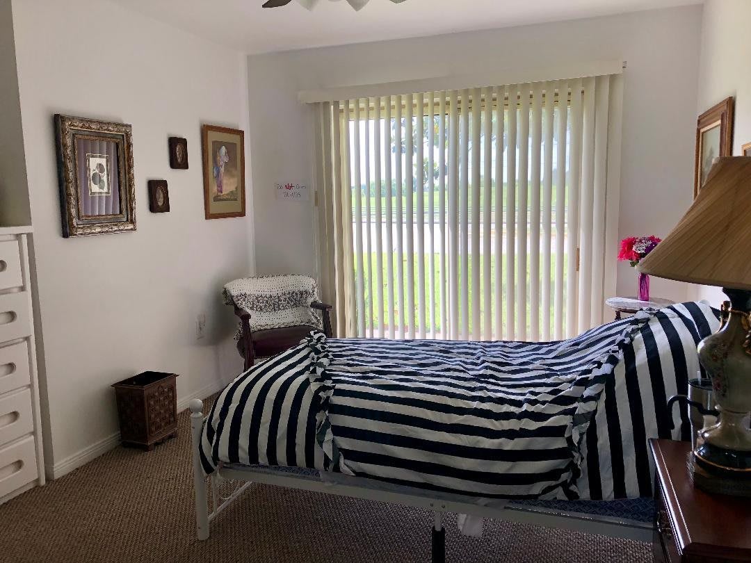 A cozy bedroom with striped bedding and wall art, featuring a large window with vertical blinds.