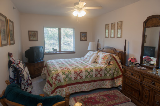 A cozy bedroom featuring a quilted bedspread, a television, and natural light coming through the windows.