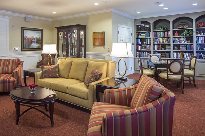 A cozy living room with a sofa, armchair, bookshelves, and decorative lamps.
