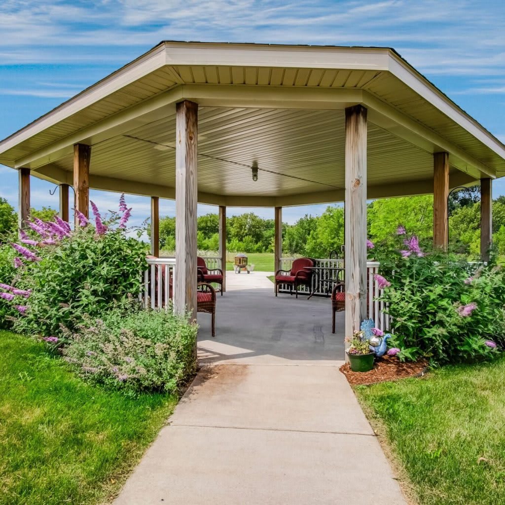 A serene gazebo surrounded by lush greenery and flowering bushes in a park setting.