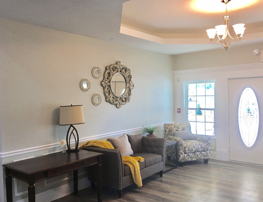 A cozy living room with modern decor, featuring a sofa, lamp, decorative mirror, and large window.