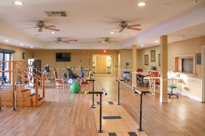 A spacious rehabilitation and exercise room with therapy equipment and wooden flooring.
