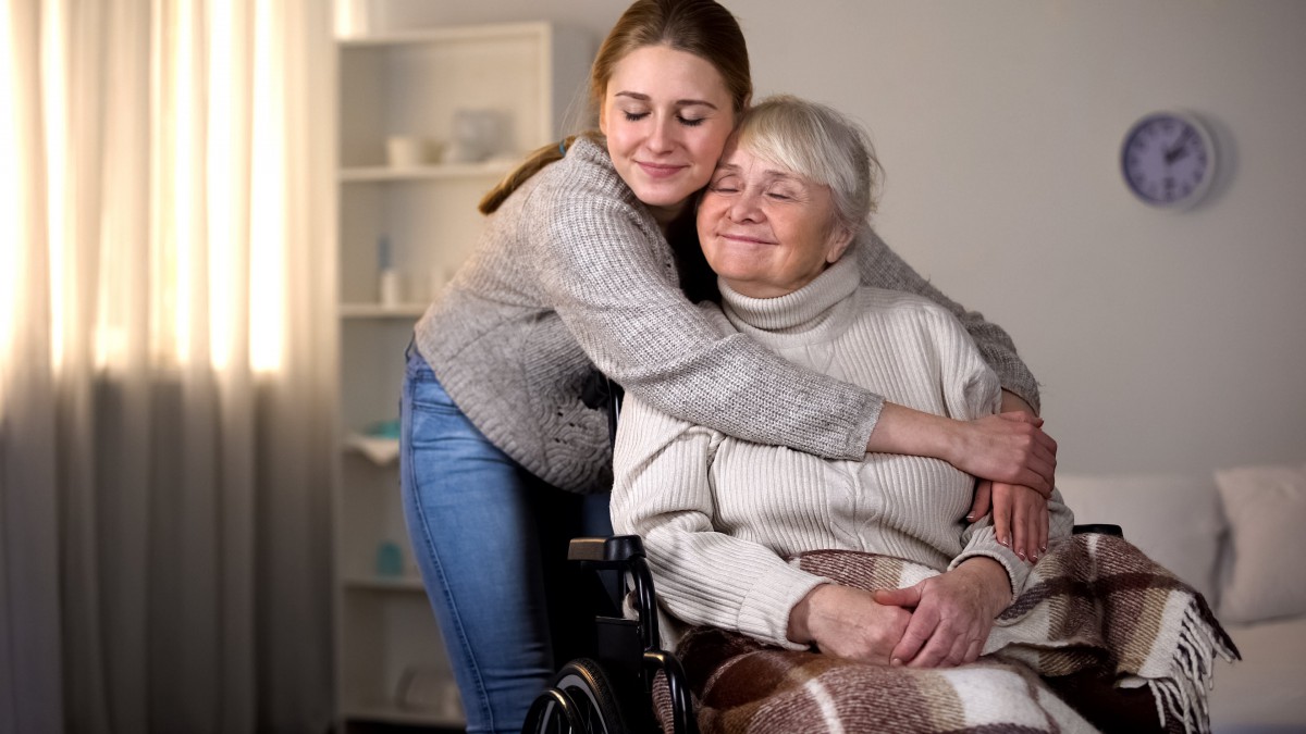A joyful moment of a young woman hugging an elderly woman in a wheelchair.