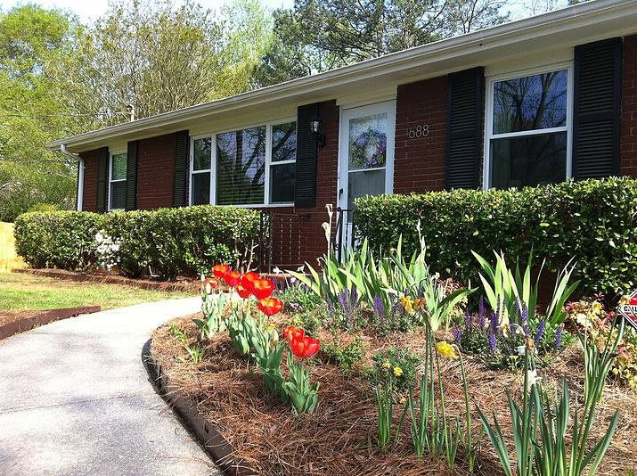 A charming house with a beautifully landscaped garden featuring vibrant flowers and a neatly trimmed hedge along the pathway.