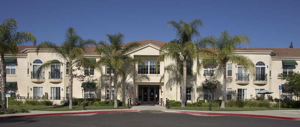A sunny day view of a building entrance surrounded by palm trees and well-maintained landscaping.