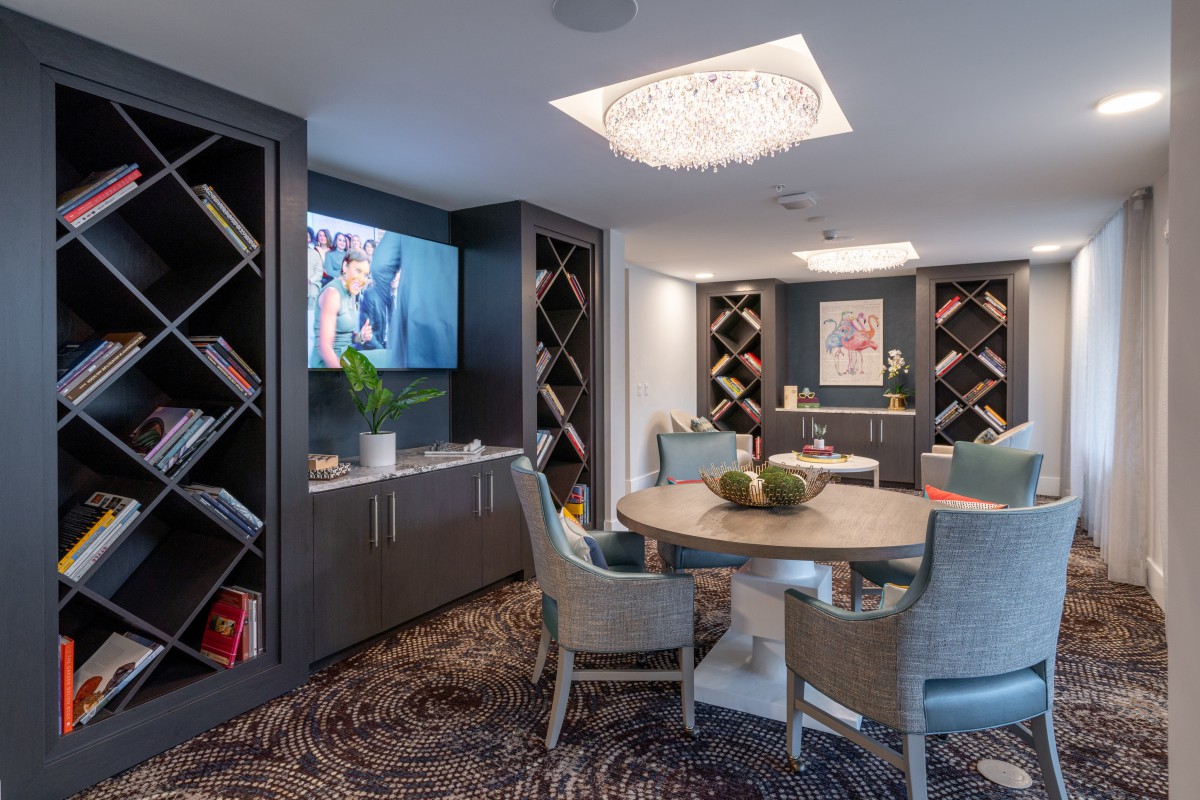 A modern living area featuring elegant seating, bookshelves, and a television under a stylish chandelier.
