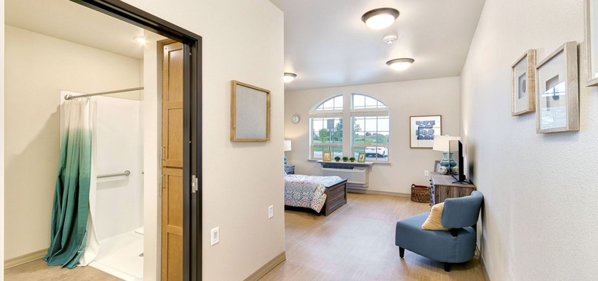 A cozy bedroom with a large window, bed, and comfortable seating area.