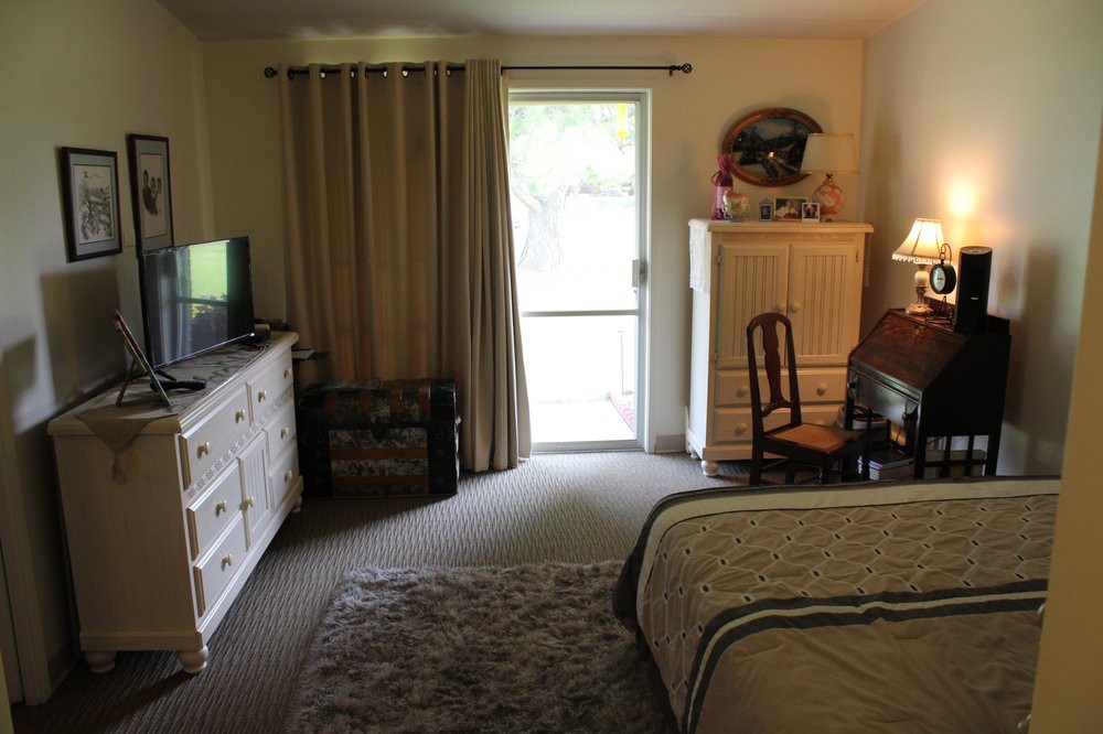A cozy bedroom with a bed, television, dresser, and desk near a window.