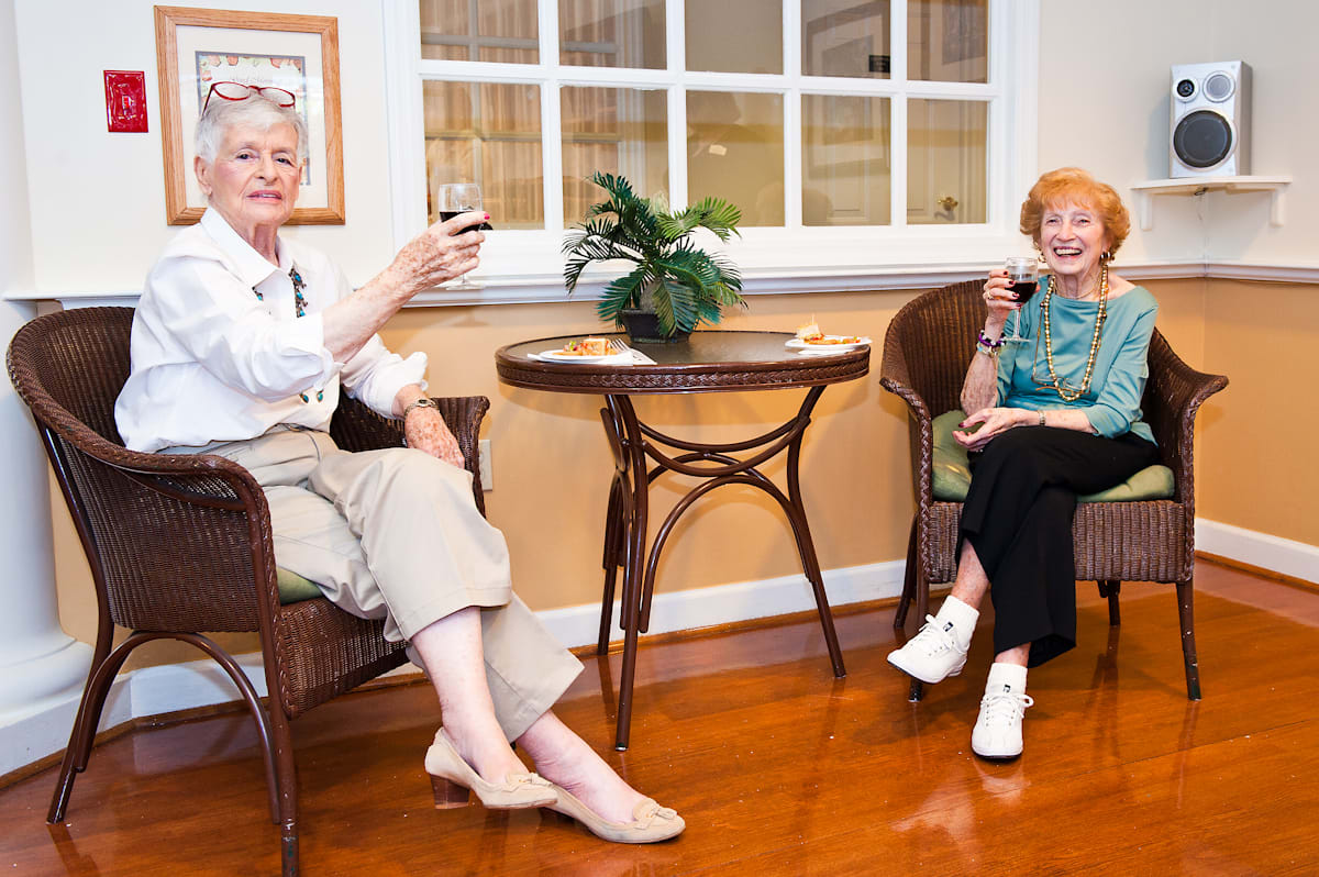 Two elderly women enjoy a glass of wine together in a cozy indoor setting.