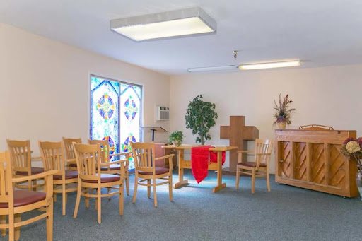 A serene chapel interior featuring wooden furniture, a cross, and stained glass windows.