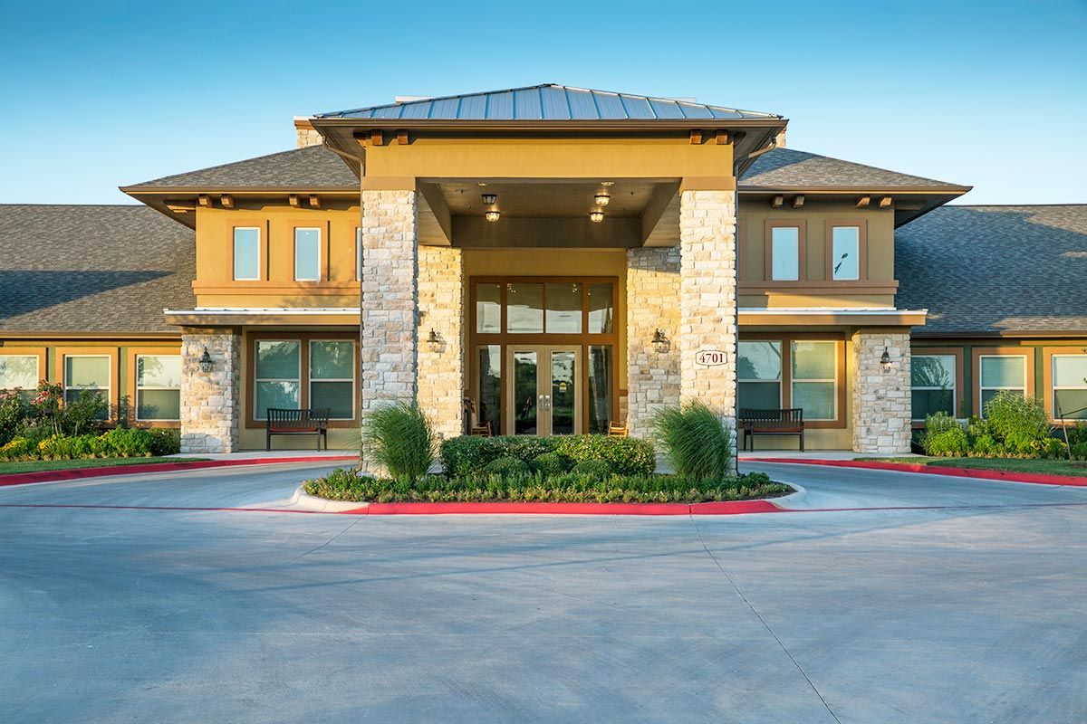 A modern building entrance with stone and wood elements, surrounded by landscaped greenery.