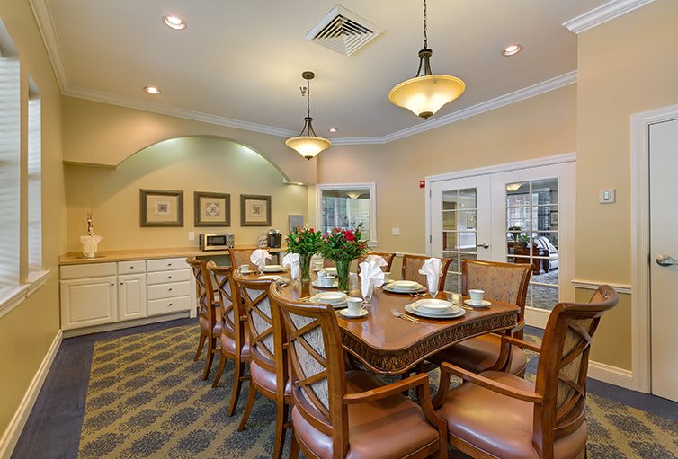 A well-lit dining room with a long table set for a meal, surrounded by wooden chairs and warm decor.